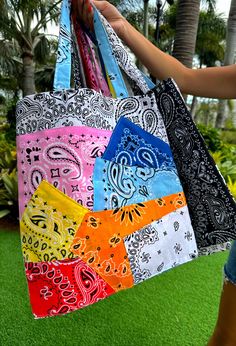 a woman holding four colorful bags in her hand on the grass with palm trees in the background