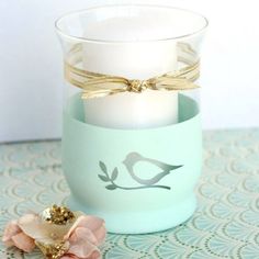 a candle holder with a bird on it next to a pink flower and a gold bow