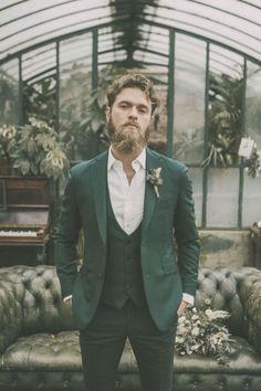 a man with a beard wearing a suit and bow tie standing in front of a couch