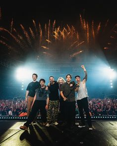 a group of people standing on top of a stage with fireworks in the sky behind them