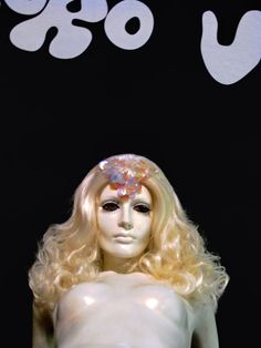 a white mannequin with blonde hair wearing a flower in her hair and the word gogo written on it