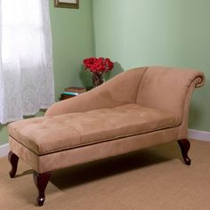 a tan chaise lounge sitting in front of a window next to a vase with red flowers