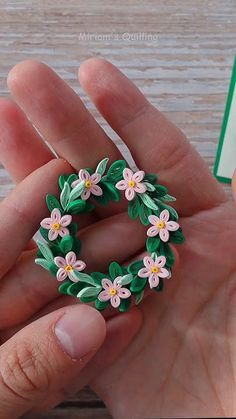 a hand holding a green and pink flower brooch