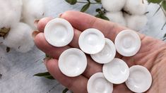 a hand is holding several white dishes in front of cotton