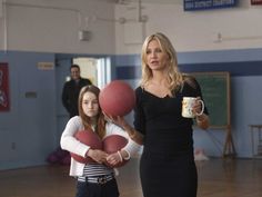 a woman holding a red ball while standing next to a girl in a black dress