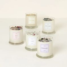 four glass candles with labels on them sitting next to each other in front of a white background