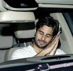 a man sitting in the back seat of a car talking on a cell phone with his eyes closed