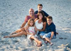 a family is sitting on the beach in front of the water and sand with their arms around each other