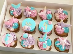 cupcakes decorated with pink, blue and purple icing in a box