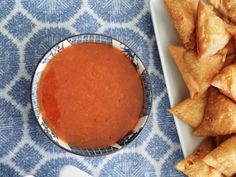 a bowl of sauce next to some pita chips on a blue and white cloth