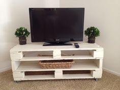 a flat screen tv sitting on top of a white wooden shelf next to a plant