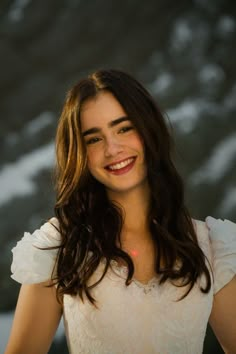 a woman with long hair smiling and wearing a white shirt in front of a snow covered background