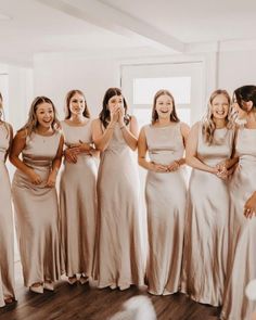 a group of women standing next to each other in front of a white wall wearing long dresses