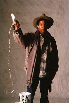 a man in a cowboy hat and scarf holding a white object with water coming out of it