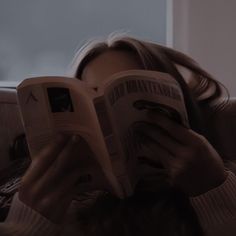 a woman reading a book while sitting in a chair with her head on the pillow