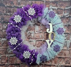 a purple and blue wreath with the word joy hanging on a brick wall in front of it