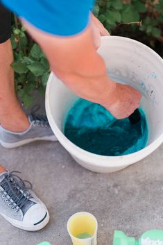 a person is mixing something blue in a white bowl with green and yellow cups next to them