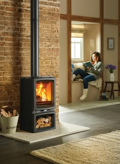 a woman sitting on a couch reading a book in front of a wood burning stove