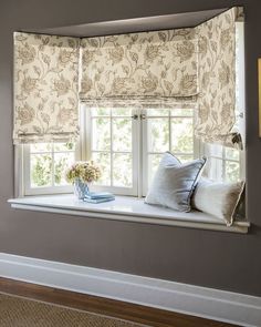 a window with some pillows on it and a vase full of flowers in the window sill