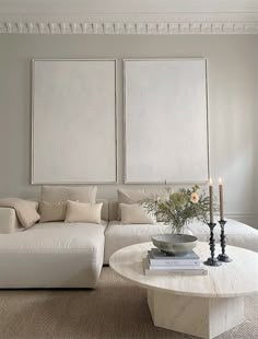 a living room filled with white furniture and two large paintings on the wall above it