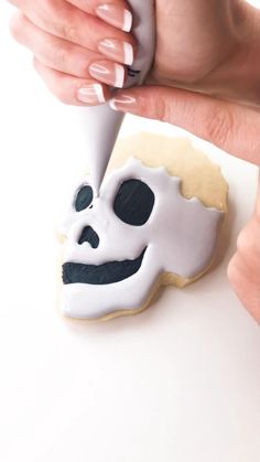 a woman is decorating a skull cookie with icing and white frosting on it