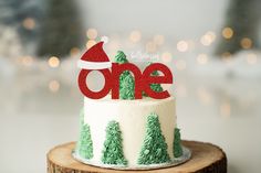 a one year birthday cake decorated with trees and a santa hat on top is sitting on a tree stump