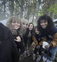 group of people posing for the camera in front of some trees and bushes with one woman holding a coffee cup