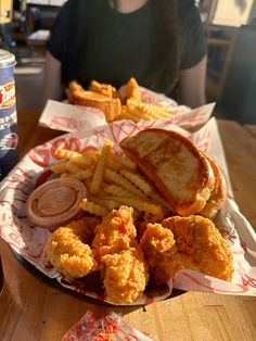 a basket filled with fried food and french fries on top of a table next to a woman