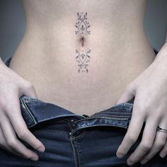 a woman's stomach with an intricate tattoo on her lower body and two hands behind her back