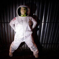 a man dressed in an astronaut suit standing next to a metal wall with his hands on his hips