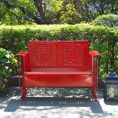 a red bench sitting in front of a bush and some bushes with two lanterns next to it