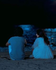 two people sitting on the beach at night