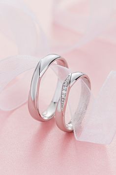 two white gold wedding rings with diamonds on pink fabric and tulle, close - up