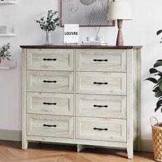 a white dresser sitting in a living room next to a lamp and potted plant