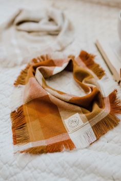 an orange and white plaid scarf sitting on top of a bed next to a cup