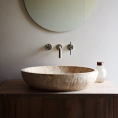 a large bowl sink sitting on top of a wooden counter next to a round mirror