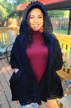 a woman standing on a deck wearing a black crochet hooded jacket and jeans