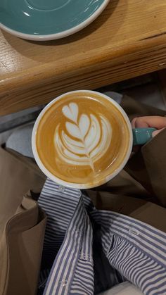 a cappuccino in a paper cup sitting on top of a wooden table