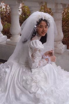 a woman in a white wedding dress sitting on a stone bench wearing a veil and tiara