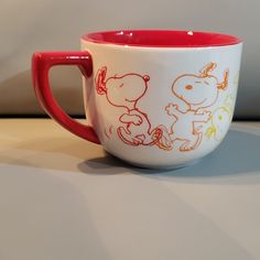 a red and white coffee cup sitting on top of a counter next to a wall