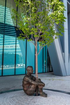 a statue sitting under a tree in front of a building with glass walls and windows