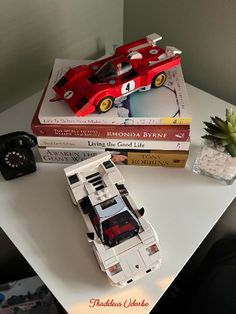 two books and a toy car are sitting on a white table next to a plant