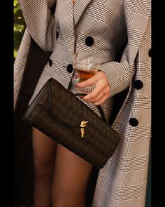 a woman holding a black purse with a drink in her hand