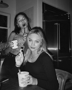 two women sitting at a table with drinks in their hands and one holding a cup