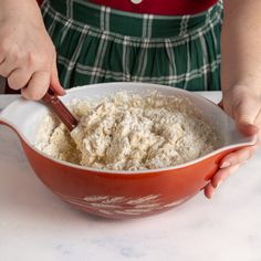 a person mixing food in a bowl on top of a white tablecloth covered counter