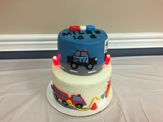 two tiered cake decorated with police cars and firetrucks on white table cloth