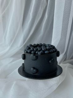 a black cake topped with blueberries on top of a white cloth covered tablecloth