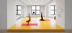 two people doing yoga on mats in a room with large windows and bright yellow flooring