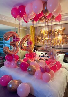 a bed topped with lots of balloons next to a table filled with pink and gold balloons