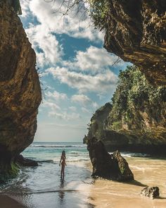 a woman is standing in the water at the beach near some large rock formations and cliffs